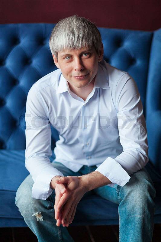 Grey haired Man sitting in blue armchair, stock photo