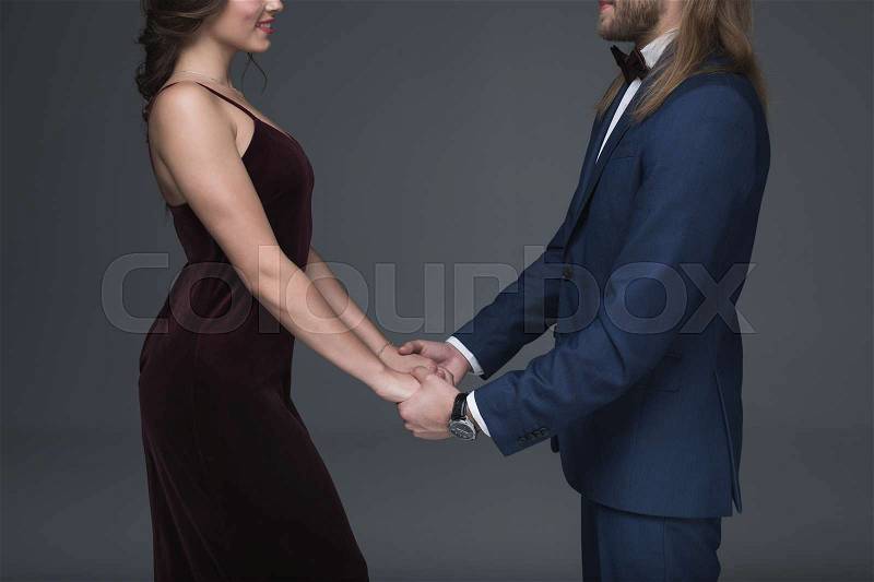 Cropped shot of young sweethearts in stylish formal wear holding hands and looking on each other, stock photo