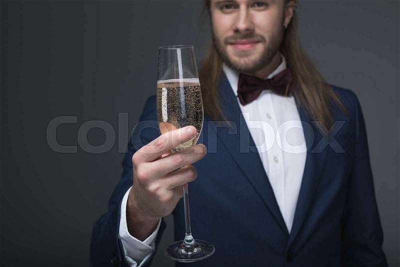 Smiling man in tuxedo holding glass with champagne and looking at camera, stock photo
