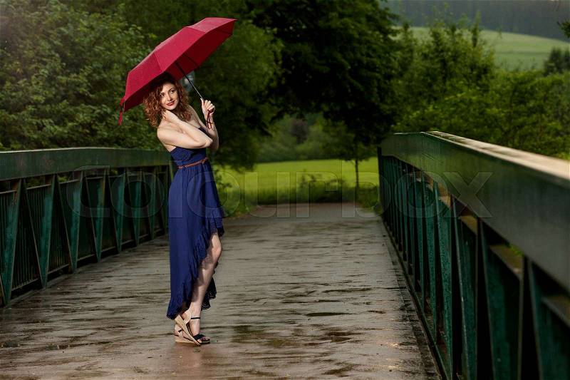 Young attractive woman with red umbrella after rain in nature, stock photo
