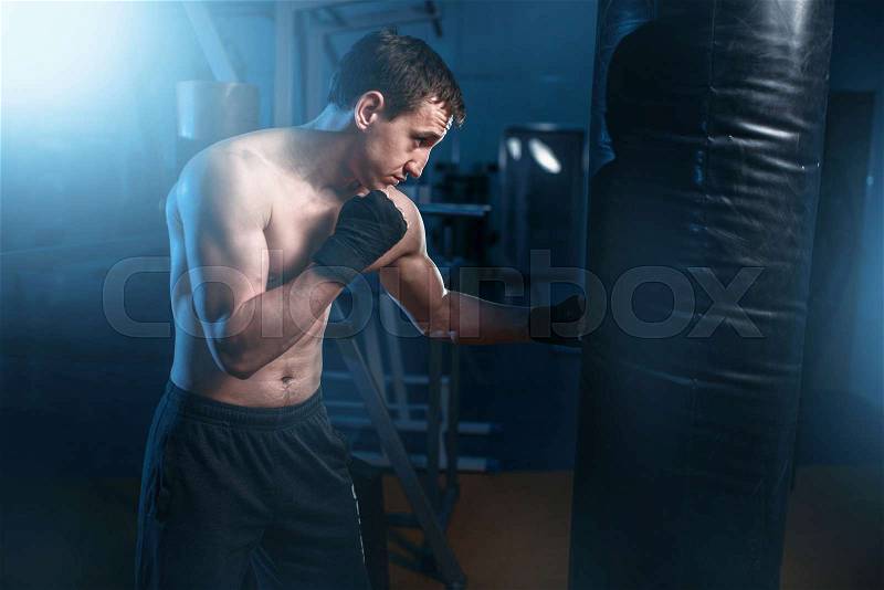 Man in black handwraps exercises with bag in gym. Boxing workout, mens sport, stock photo