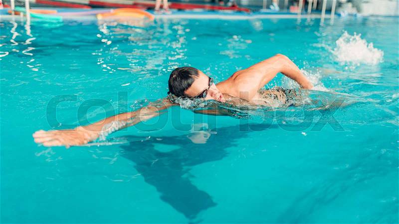 Athletic swimmer in glasses swims in indoor swimming pool. Aqua sports exercise, stock photo