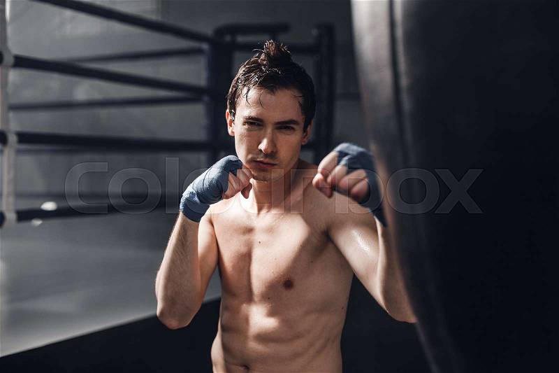 Portarait of young boxer man in boxing wraps with punching bag. The concept of a healthy lifestyle, stock photo