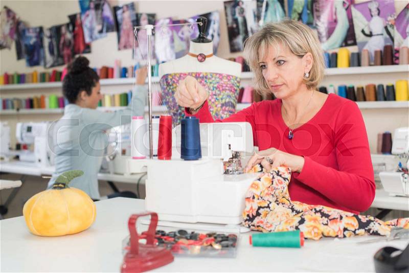 Happy attractive woman seamstress working on sewing machine, stock photo