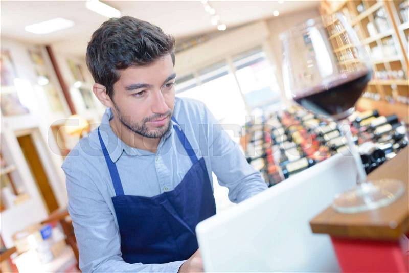 Handsome sommelier ordering wine on computer at store, stock photo