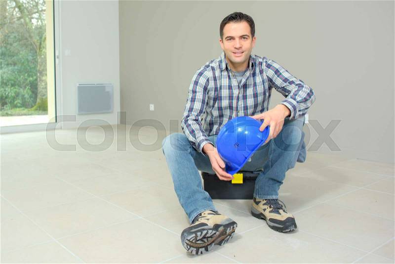 Smiling builder sitting on the floor in empty home, stock photo