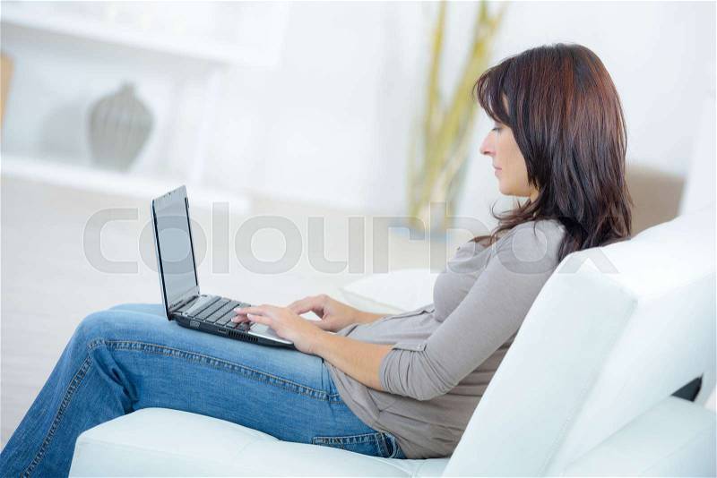 Pretty woman sitting on couch with laptop, stock photo