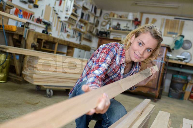 Happy female carpenter holding wooden plank, stock photo
