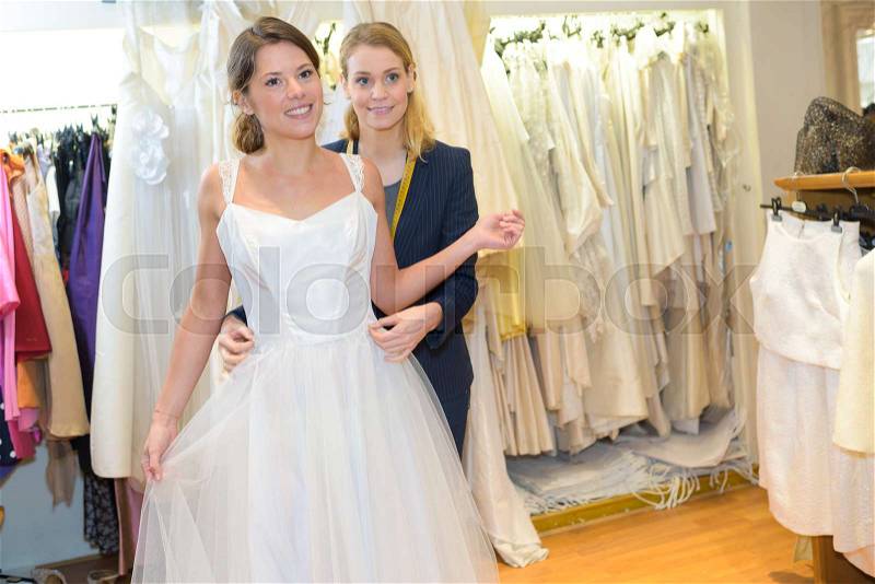 Female trying on wedding dress in a shop with assistant, stock photo