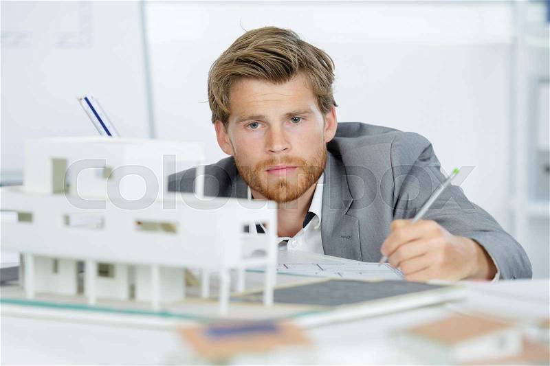 Young architect looking down at project at table in office, stock photo