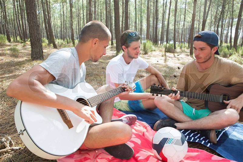 Friends playing guitar at a forest, stock photo