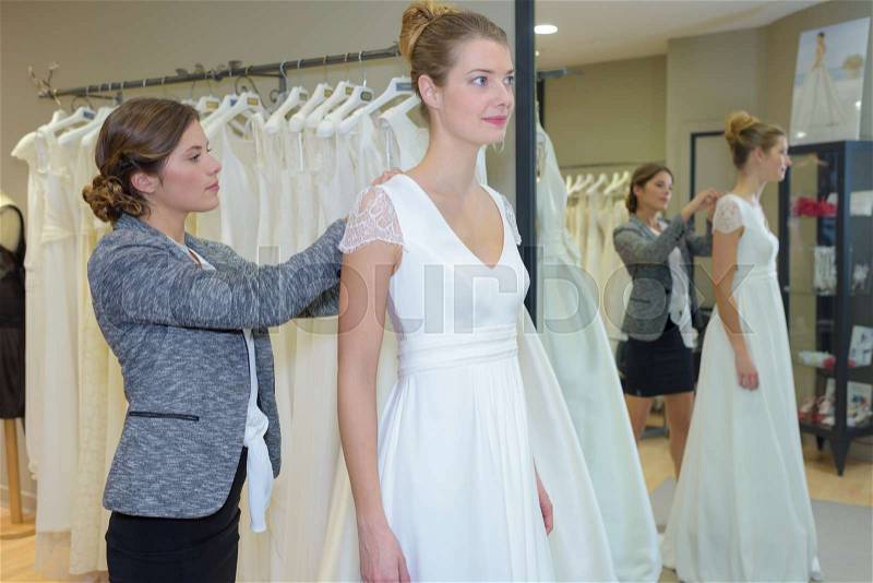Female trying wedding dress in a shop with shop assistant, stock photo