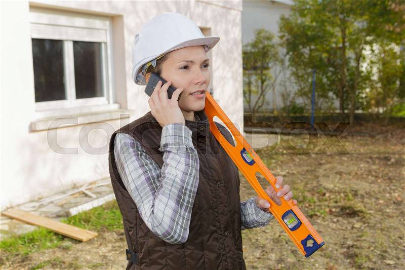 Female construction worker with level at construction site, stock photo