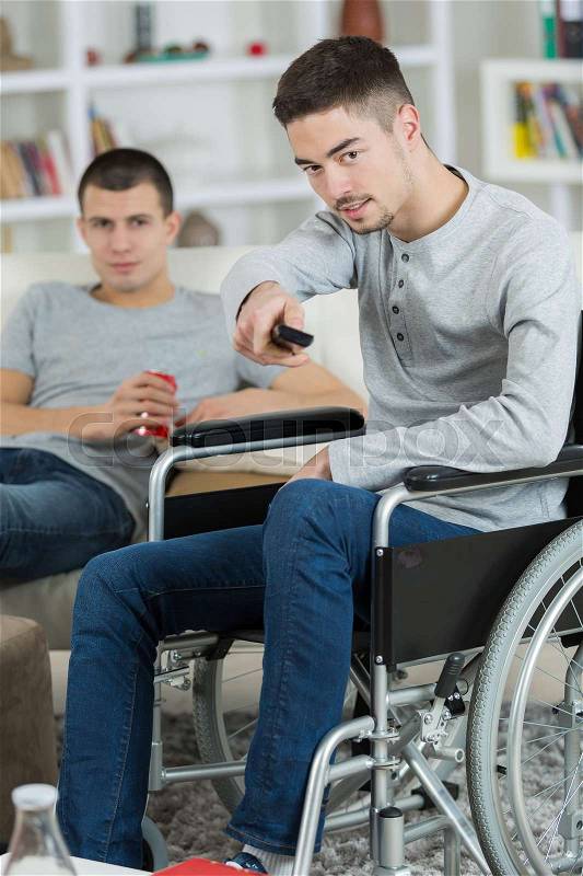 Disabled young man watching television with friend, stock photo