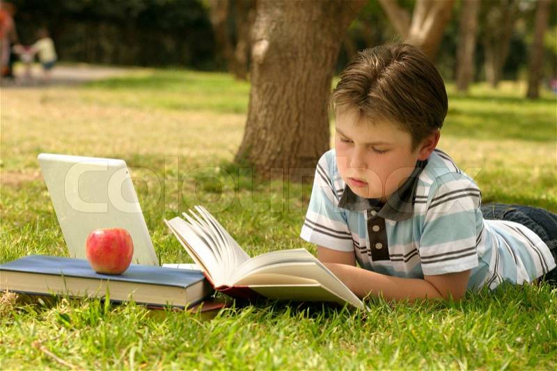 A child student relaxes or studiesby reading a book in the park, stock photo