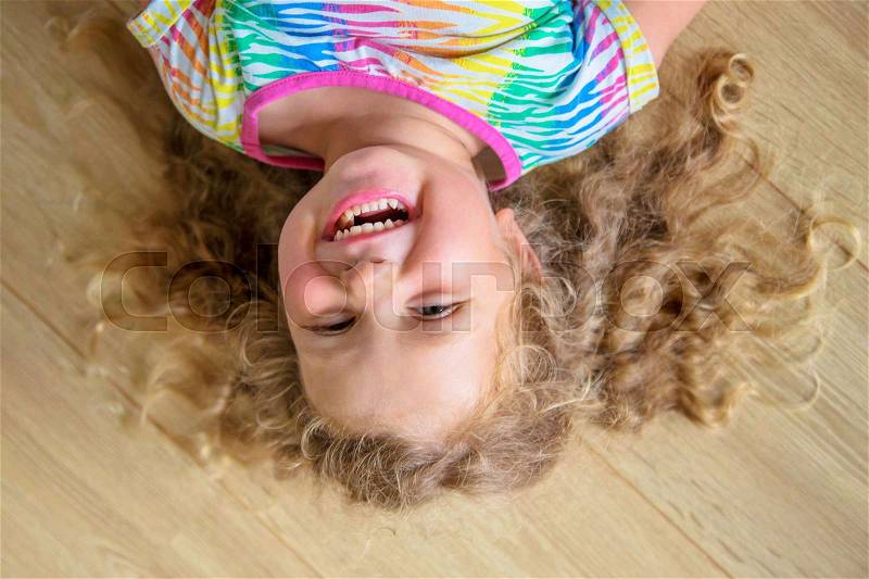 Happy little girl with blond curly hair upside down. Child smiling and laughing, stock photo