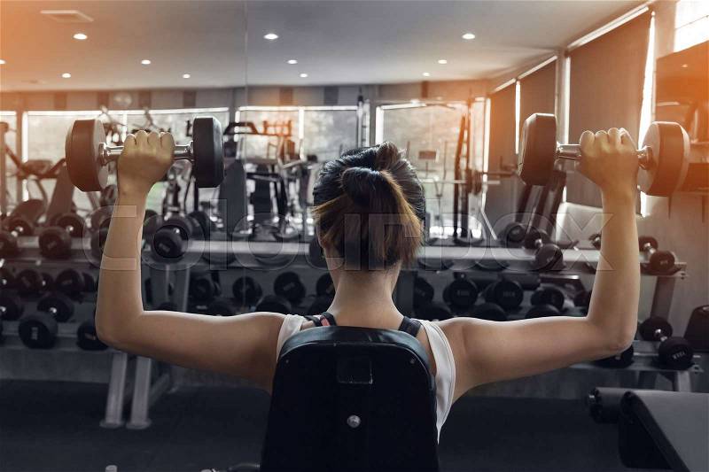 Woman weight lifting dumbbell bodybuilding in workout fitness gym, stock photo