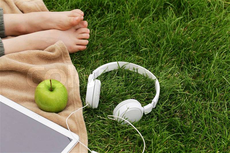 Headphones, electronic tablet and green apple for picnic in park on green grass, stock photo