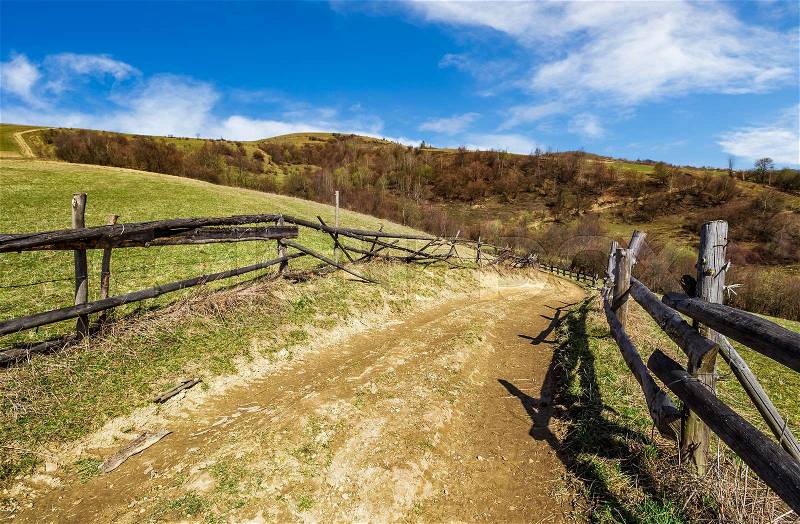 Wooden fence by the road in rural area. springtime countryside landscape in mountains with grassy meadows. beautiful sunny weather, stock photo