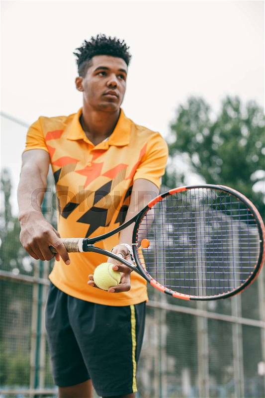 Low angle view of determined young black man playing tennis. Tennis player posing in front of a tennis court, stock photo