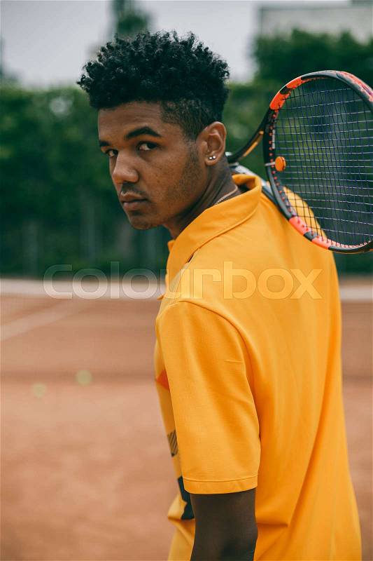 Portrait of serious african man holds a tennis racket on his shoulder. Back view portrait of a man playing in tennis outdoors, stock photo