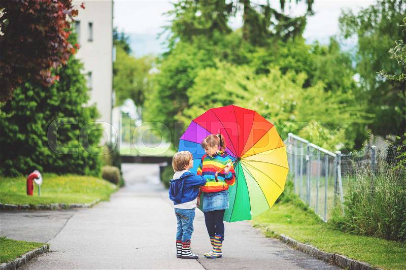 Two adorable kids playing outdoors with big colorful umbrella, stock photo
