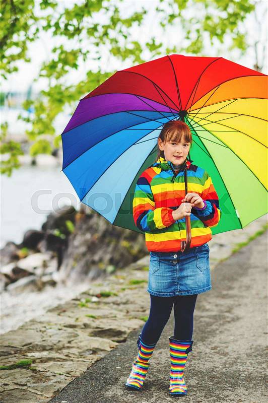 Outdoor portrait of pretty little kid girl with big colorful umbrella, wearing rain jacket and boots, weather concept, fashion for kids , stock photo
