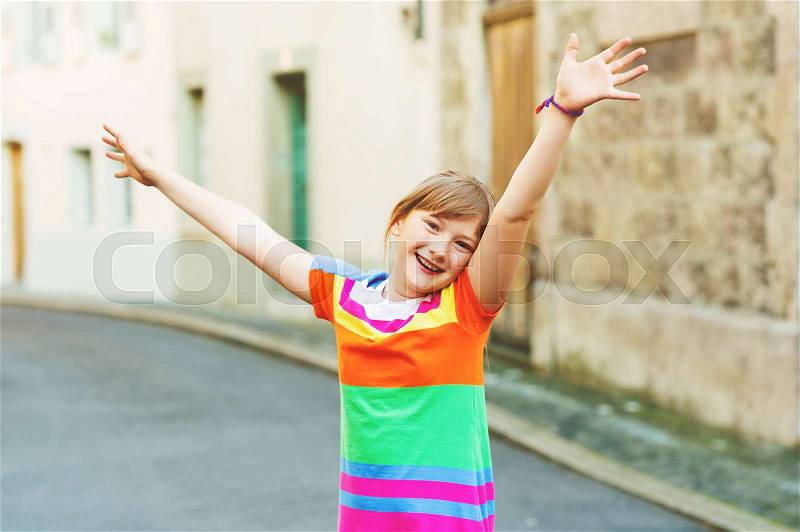 Happy smiling joyful kid girl with arms up playing on the street, stock photo
