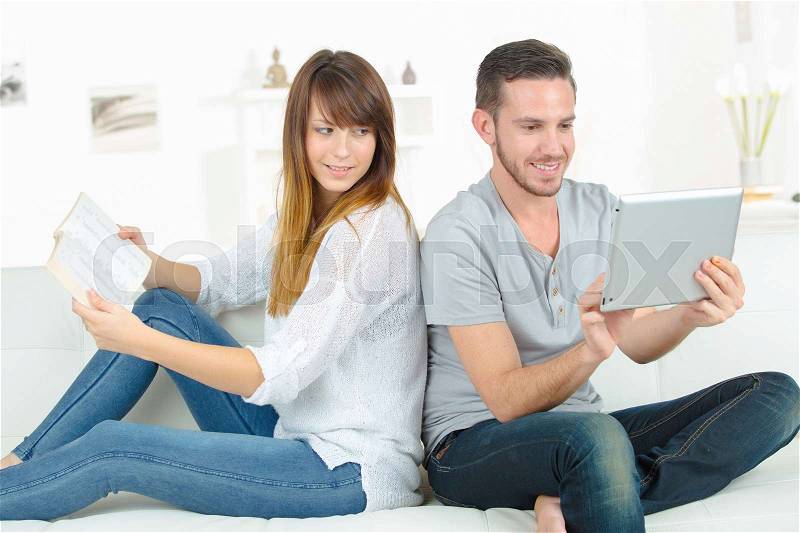 Couple on sofa with digital tablet and book, stock photo