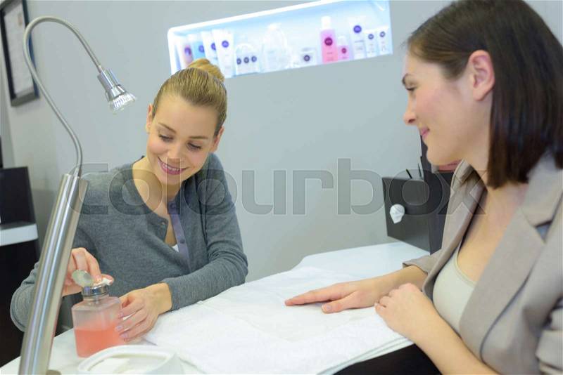 Attractive nail salon worker giving a manicure to one customers, stock photo
