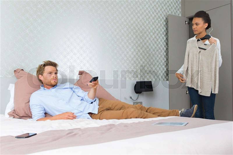 Boyfriend watching tv while girlfriend tries outfit, stock photo