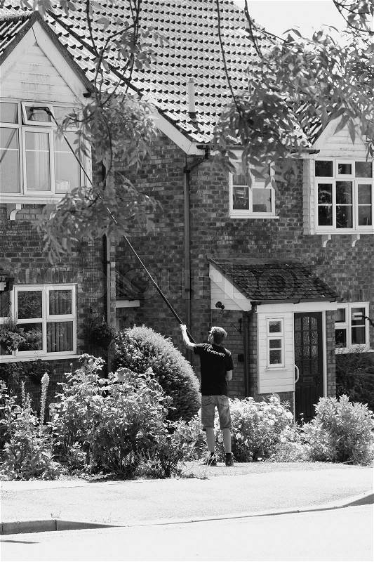 The window cleaner is busy with the windows from the front of the house in the residential area in the village Tenterden in England in the summer in black and white, stock photo