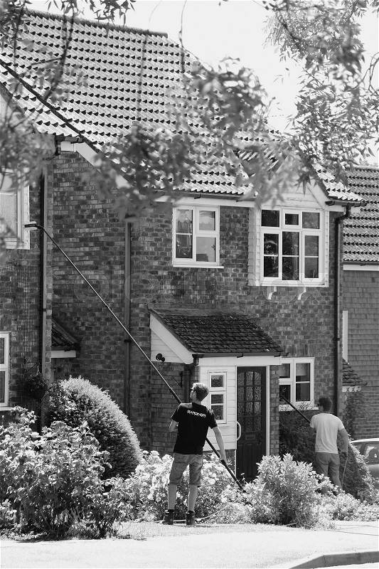 The two window cleaners are busy with the windows from the front of the house in the residential area in the village Tenterden in England in the summer in black and white, stock photo