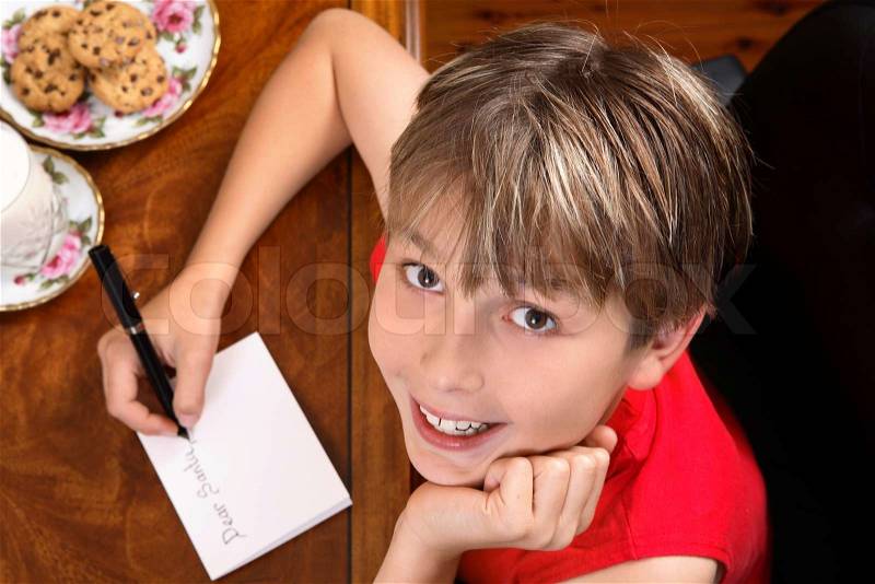 A child sitting at a desk writing a letter for Santa or Christmas card, stock photo