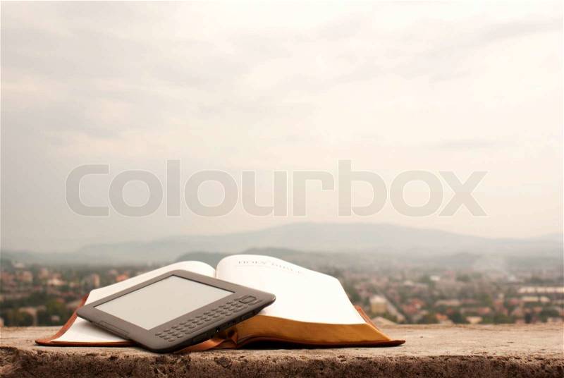 Electronic book reader laying on the book outdoors, stock photo