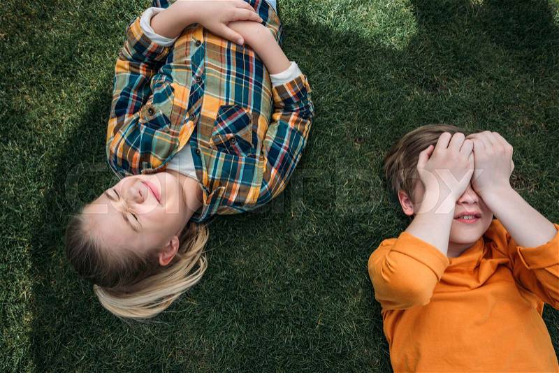 Above view of adorable kids sunbathing while lying on grass, stock photo
