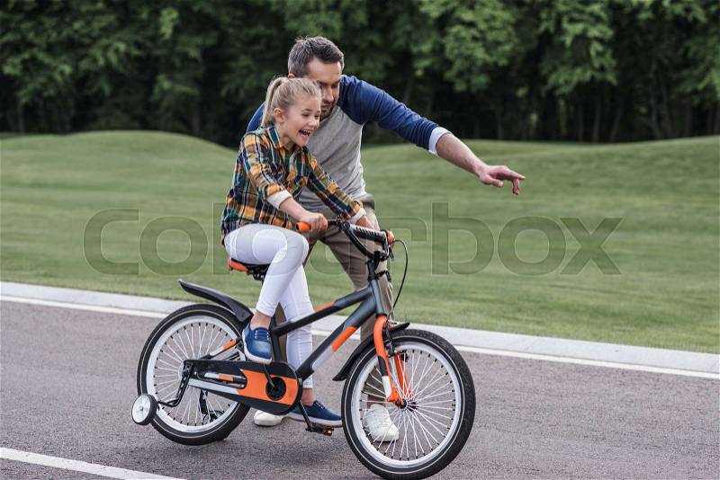 Young father teaching his little daughter riding bicycle on asphalt road, stock photo