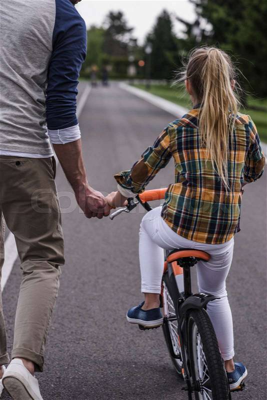 Cropped shot of father teaching his little daughter riding bicycle on asphalt road, stock photo