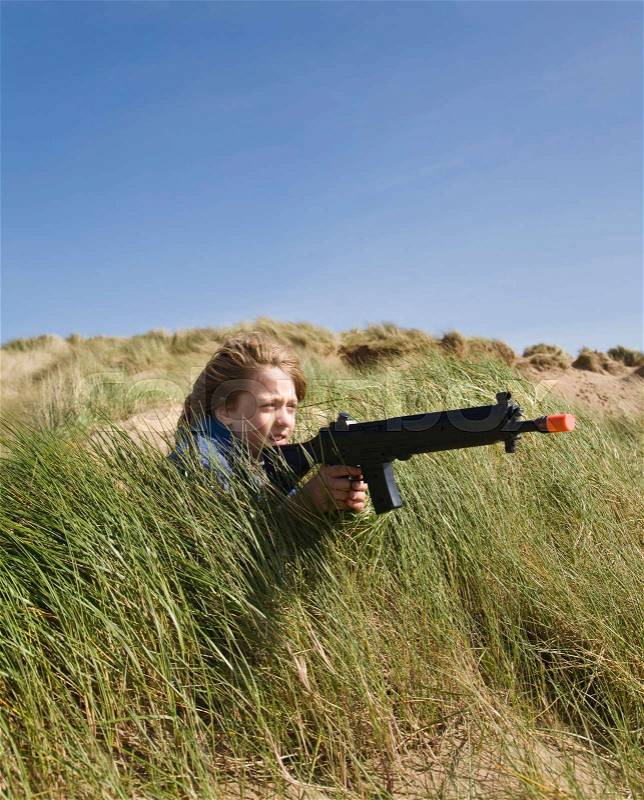 Boy in dunes with toy gun, stock photo