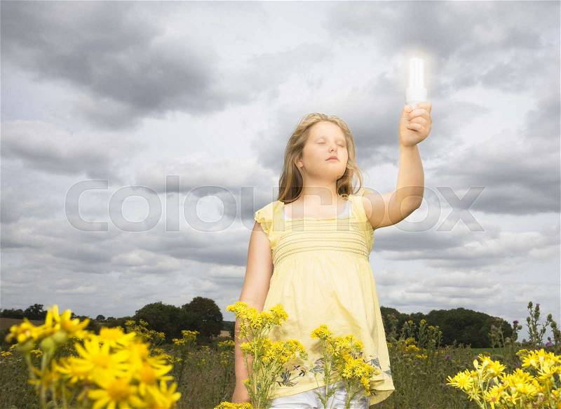 Girl with energy saver bulb in field, stock photo
