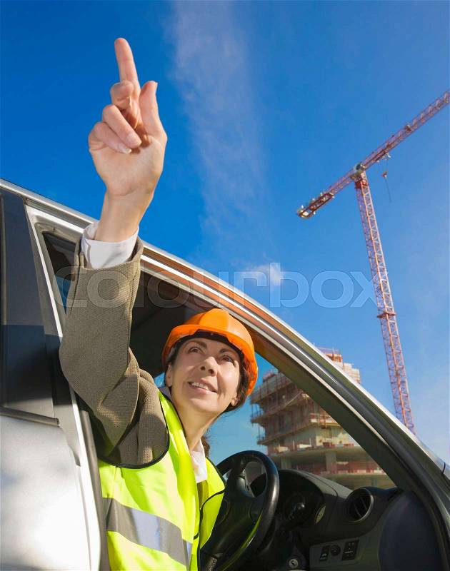 Woman pointing from car at building site, stock photo