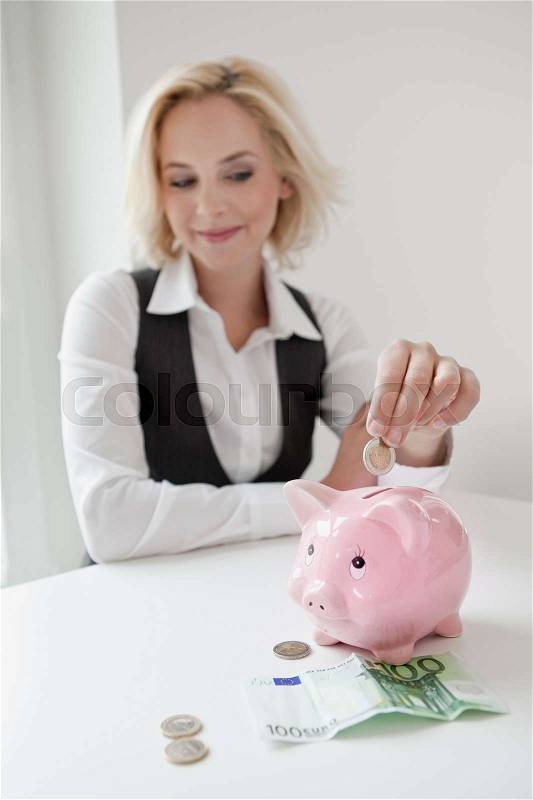 Woman dropping money into piggy bank, stock photo