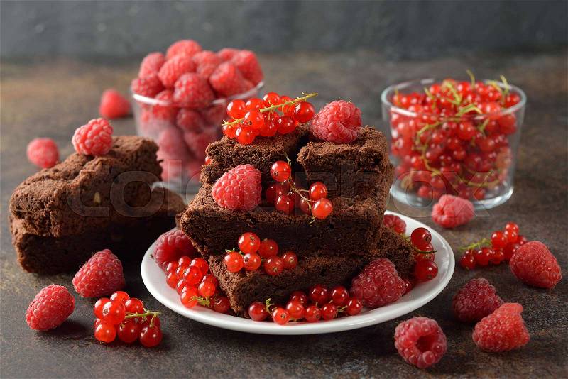 Chocolate brownies with raspberries and currants on a brown background, stock photo