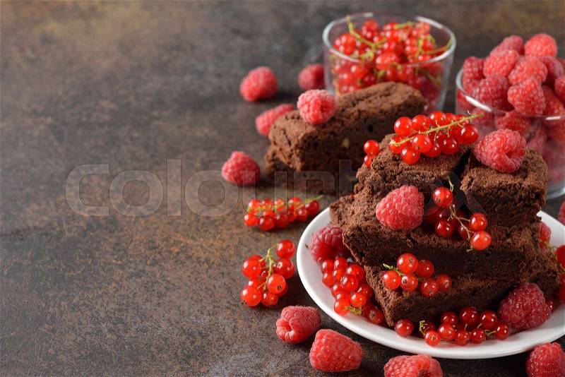 Chocolate brownies with raspberries and currants on a brown background, stock photo