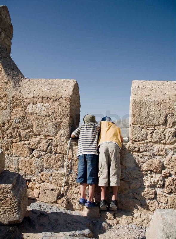 Two boys looking over wall at view, stock photo