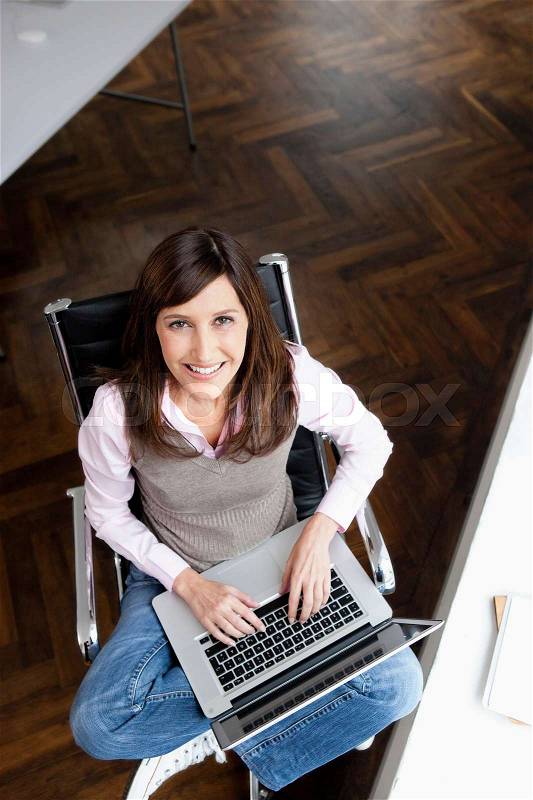 Woman typing on laptop looking to camera, stock photo