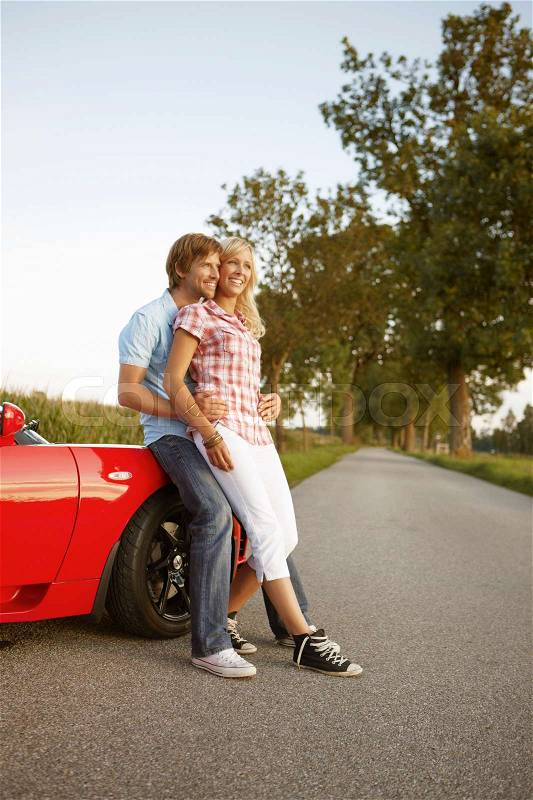 Couple sitting on electric sports car, stock photo