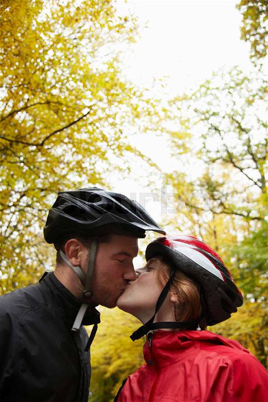 Couple wearing cycle helmets kissing, stock photo