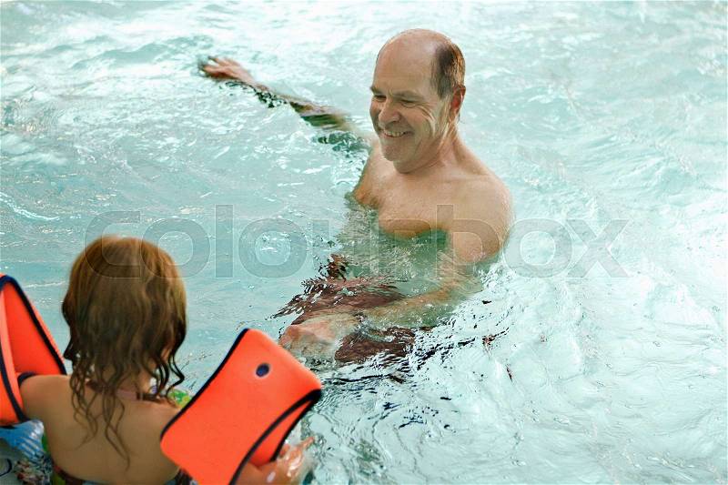 Older man swimming with grandchild, stock photo