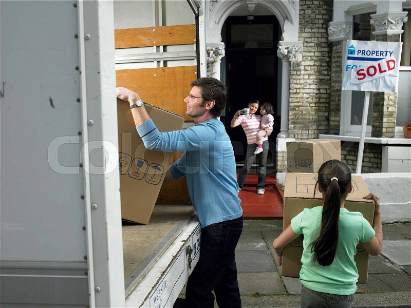 Family unpacking boxes from moving van, stock photo